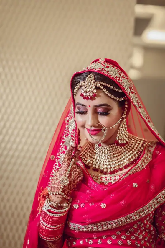 A bride in a red and gold lehenga looking down