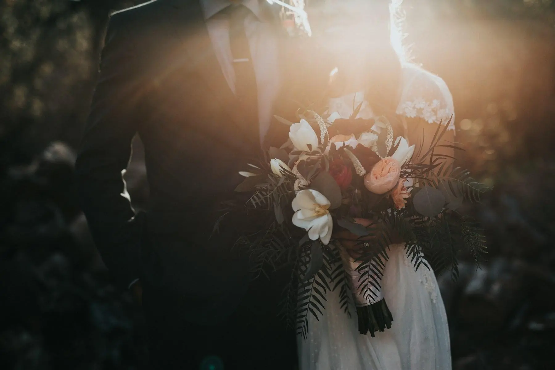 A couple seen from behind in late sunlight, the bride holding a bouquet
