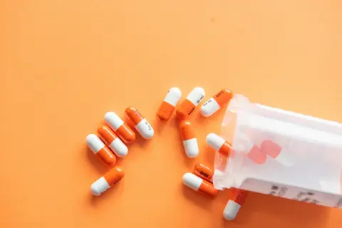 Orange and white capsules spilling from a bottle