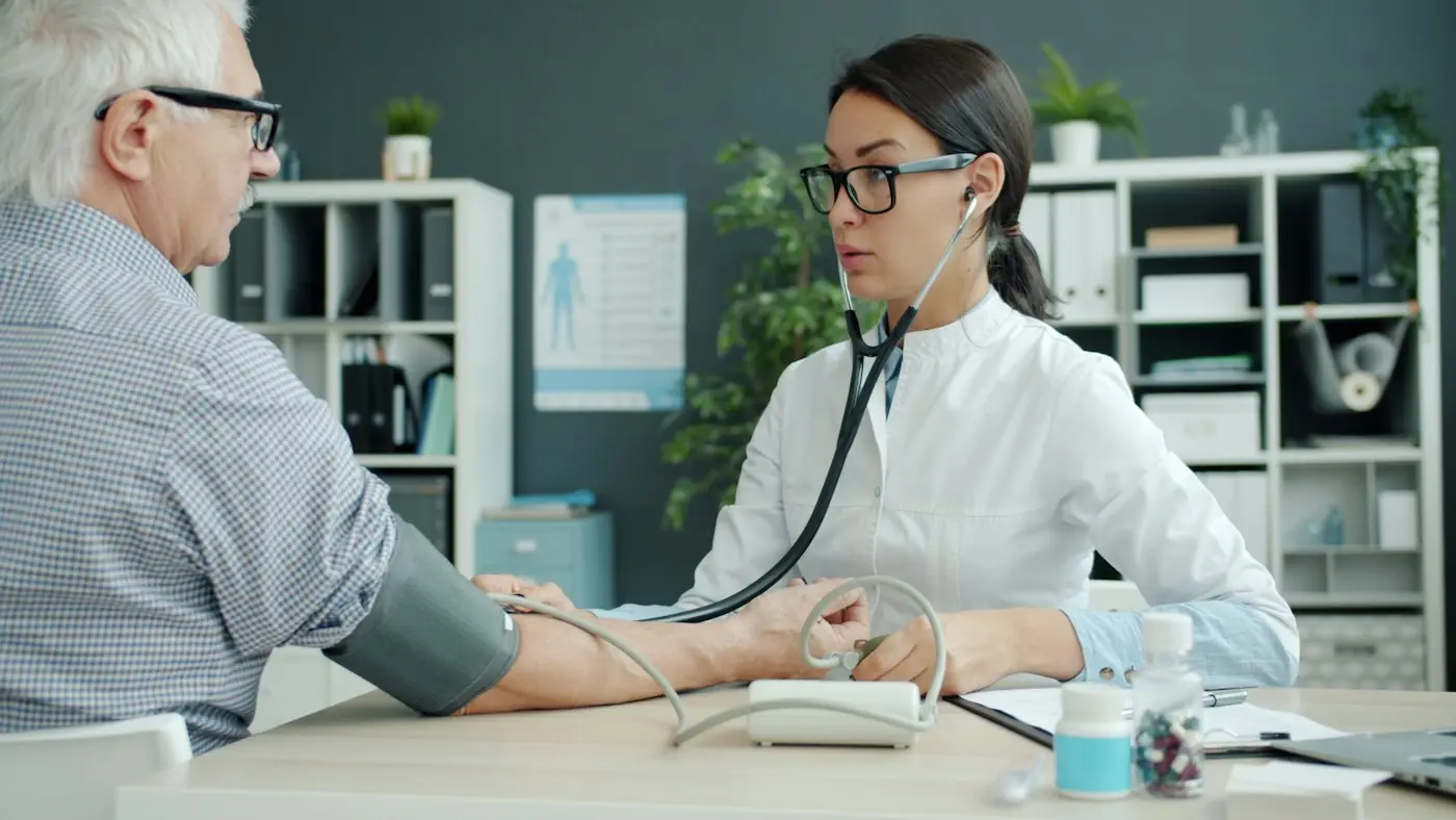 A doctor taking an older patient's blood pressure across a desk
