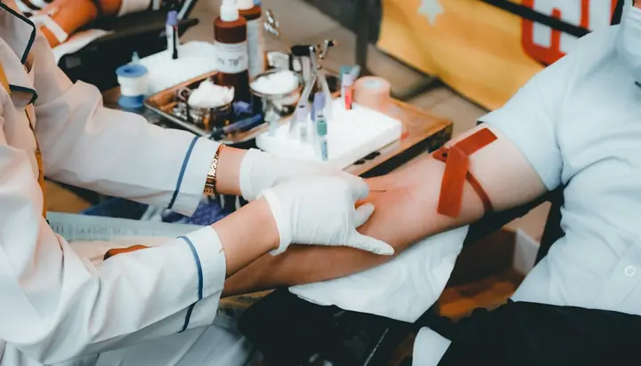 A gloved health worker drawing blood from a person's arm