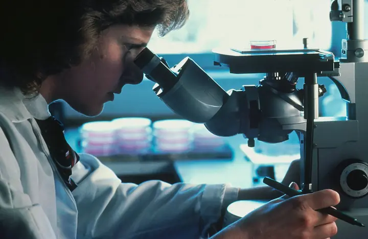 A person in a lab coat looking through a microscope